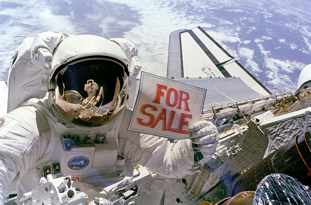 Dale Gardner holding a "For sale" sign after recovering two satellites (Photo NASA)
